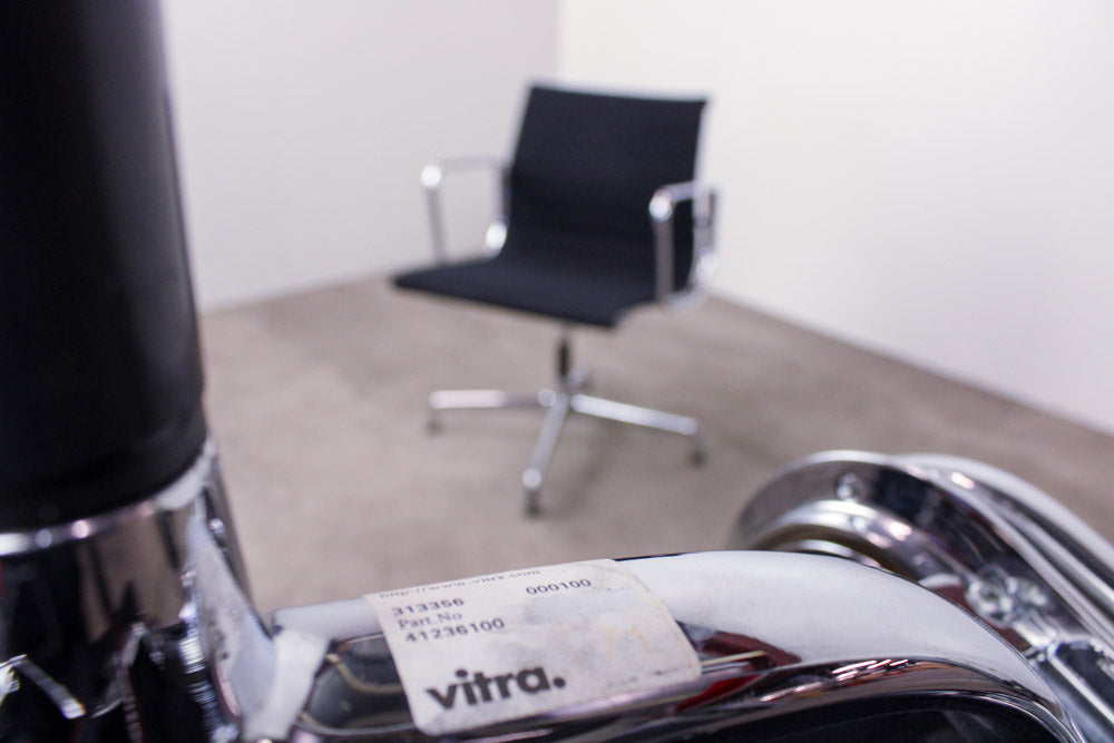 Vitra EA108 Aluminium Chair im Raum, Etikett im Vordergrund, Gesamtansicht unscharf